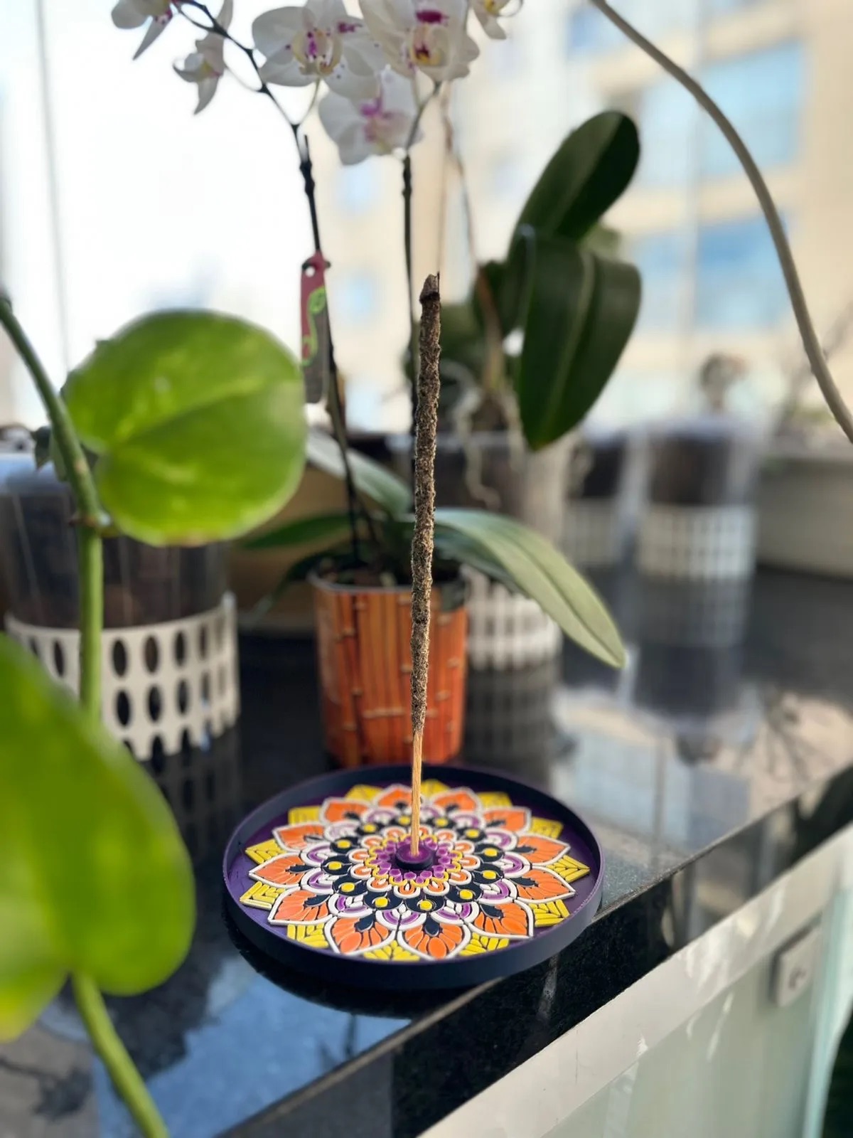 Base decorativa em mandala colorida sob um vaso de orquídea